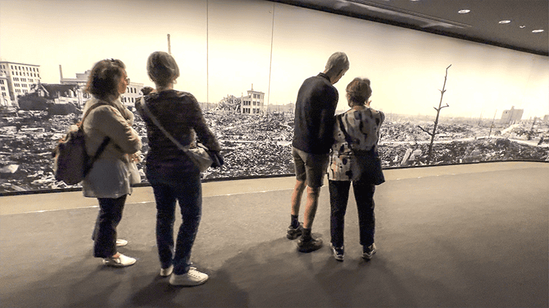 people in a museum looking at a large photo of a city destroyed by a bomb