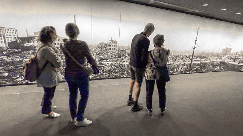 people looking at a large photo of a destroyed city on a wall in the Hiroshima peace museum