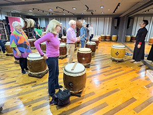 people in a class standing by large wooden drums