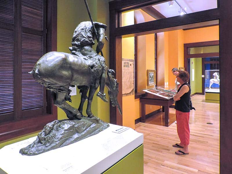 woman looking at an exhibit of a bronze statue of a horse and native American - one of the things to do in the finger lakes
