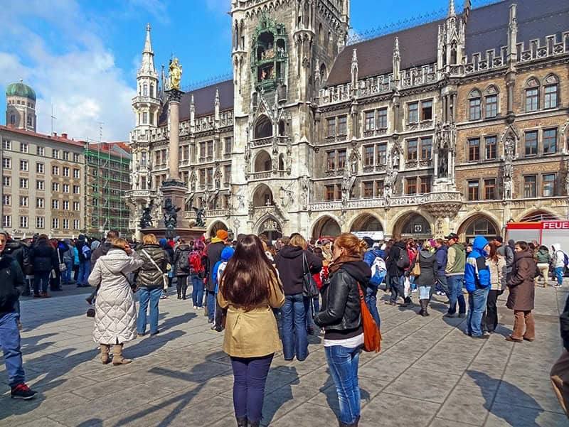 people gathered on a city square surrounded by old buildings